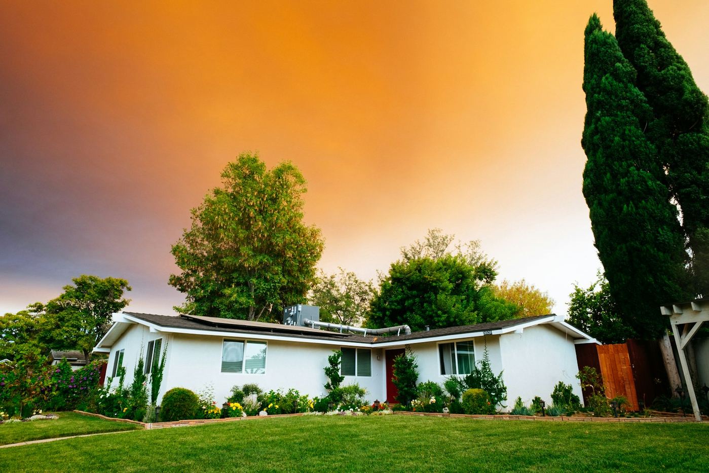 Single-story ranch home with a red door and solar panels at golden hour.