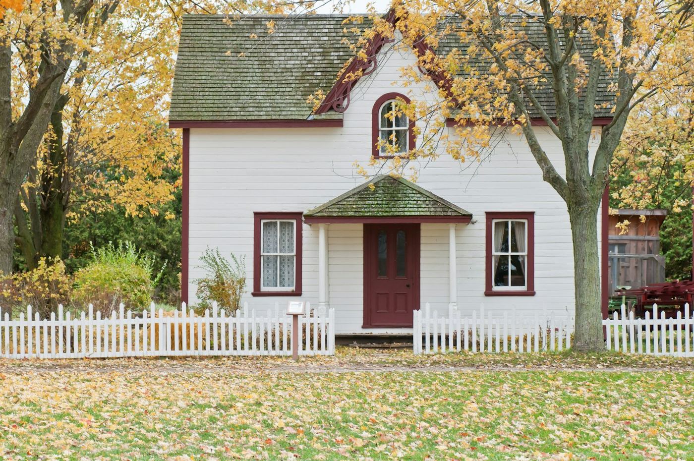 White family home with a picket fence and autumn trees in a quiet neighborhood.