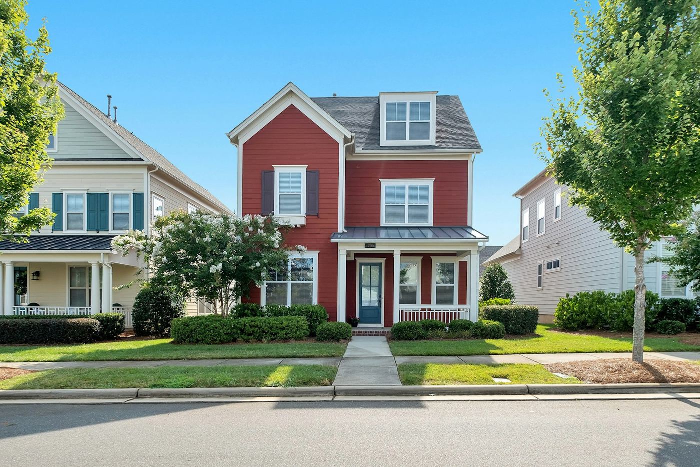 Newer two-story suburban home with a teal door, sidewalk, and neighboring houses.